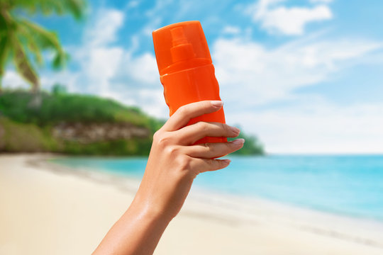 Female hand holding sunscreen cream  bottle  on beach background