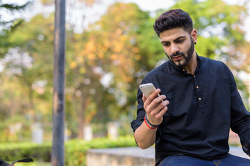 Young handsome Indian man using mobile phone while sitting on co