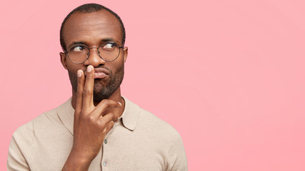 Studio shot of pensive experienced businessman looks thoughtfully aside, tries to develop new business investment plan, thinks about work all day time, poses against pink background with copy space