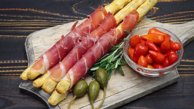 italian grissini with prosciutto, capers and pepper on wooden cutting board