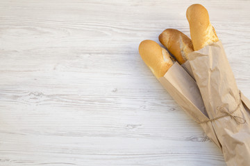 French baguettes in paper bags on white wooden table, top view. Copy space.