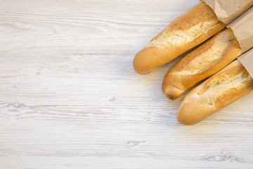 French baguettes in paper bags on white wooden table, top view. Copy space.