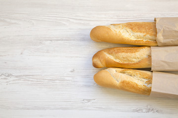 French baguettes in paper bags on white wooden table, top view. Copy space.