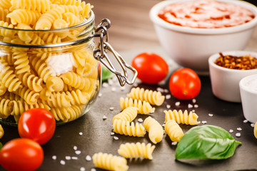 Raw pasta with spices on black stone on wooden background
