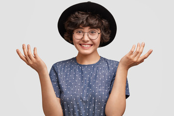 Pleasant looking female in hat with clueless hesitant expression, has positive smile on face, can`t...