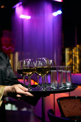 Waiter serving champagne and water on a tray. Waiter welcomes guests at the party in restaurant