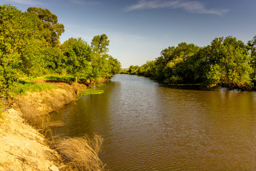 Fototapeta premium Landscape with the river and green vegetation of trees and plants on the river banks. Beautiful clear blue sky and the water of the river. River Sorraia in Benavente, Portugal