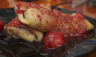 Rolled up pancakes filled by cottage cheese and strawberry jam over with berries