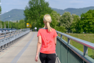 Blond woman jogging across a pedestrian bridge