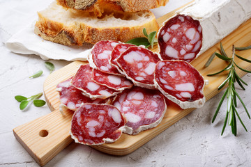 Sliced salami on cutting board with bread, rosemary and sage - obrazy, fototapety, plakaty