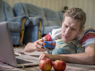 young man lying with the cup of tea in front of laptop