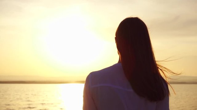 Young woman in white shirt walking at sunset on lake in slow motion. Female traveler turning around and smiling to her boyfriend