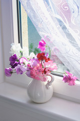 Sweet pea flowers in a vase on the window sill with delicate white curtain, beautiful still life
