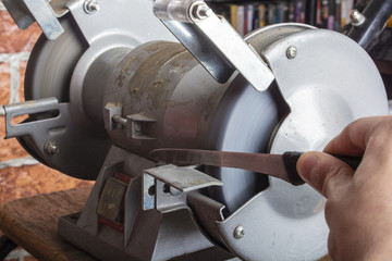 Knife sharpener and hand with blade on wooden table, closeup