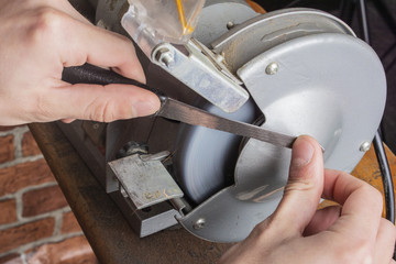 Knife sharpener and hand with blade on wooden table, closeup