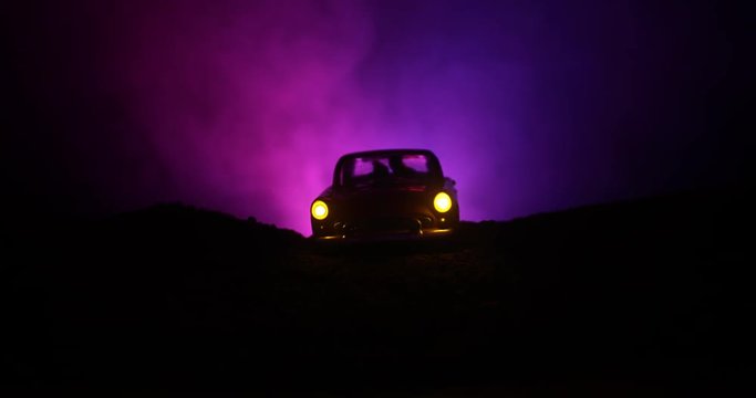 Silhouette of car with couple inside on dark background with lights and smoke. Romantic scene or Silhouette of old vintage car in dark foggy toned background with glowing lights. Slider shot