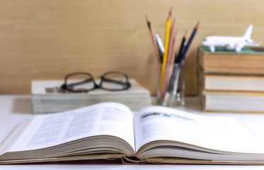 Open hardback or textbook with glasses, and stationary placed on the table.