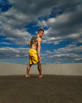 Tricking on street. Martial arts. Man stands in rack for roundhouse kick barefoot. Shooted from bottom foreshortening against sky.