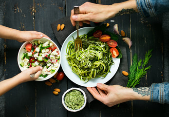 Woman hands holds zucchini raw vegan pasta with avocado dip suace, spinach leaves and cherry tomatoes on plate. On dark background. Vegetarian healthy food