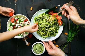 Woman and baby hands holds zucchini raw vegan pasta with avocado dip suace, spinach leaves and...