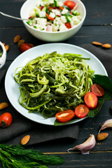 Zucchini raw vegan pasta with avocado dip suace, spinach leaves and cherry tomatoes on plate. On dark background. Vegetarian healthy food