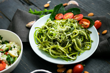 Zucchini raw vegan pasta with avocado dip suace, spinach leaves and cherry tomatoes on plate. On dark background. Vegetarian healthy food