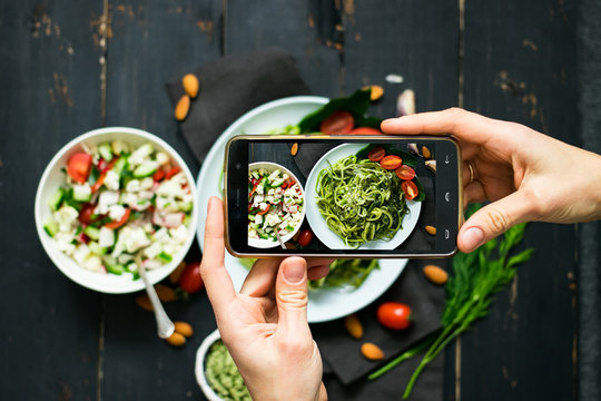 Phone photography of food. Woman hands take photo of lunch with smartphone for social media. Raw vegan zucchini spaghetti with avocado sauce. vegetarian healthy dinner 