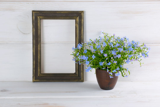 Forget-me-not flowers bouquet in clay cup and photo frame on white wooden shabby board