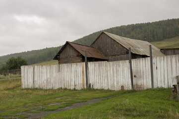 Obraz premium Heavy grey clouds in the cold autumn sky over village. Old forgotten ruined local farm and low fences in the mountains and fields. Travelling on the suburb roads. People living