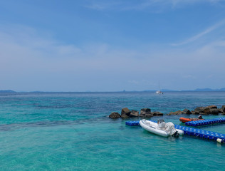 Beautiful sea, crystal clear water. White Inflatable Lifeboat with small motor in the sea. There are many stone here near the coast at the island in Thailand.