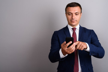 Businessman wearing suit while using mobile phone against gray b