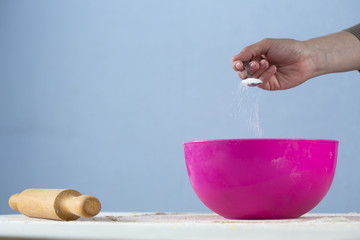 kneading dough in a bright pizza dish. female hand close-up adds sugar with a teaspoon and a wooden rolling pin next to it on a table sprinkled with flour