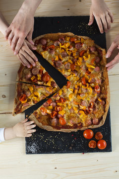 family  very fond  pizza. the hands of children and adults over homemade pizza made by own hands, on a stone dish and white table