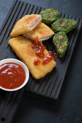 Black wooden serving board with chicken cordon bleu, vegetable nuggets and sauce, selective focus, studio shot