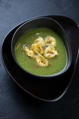 Cream-soup with broccoli and tortellini served in a black bowl, selective focus, vertical shot