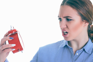 Portrait of upset Caucasian woman looks in shock at red alarm clock over white background.