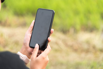 Asian woman wearing smartwatch and using smartphone in her vacation time at green field in selective focus.