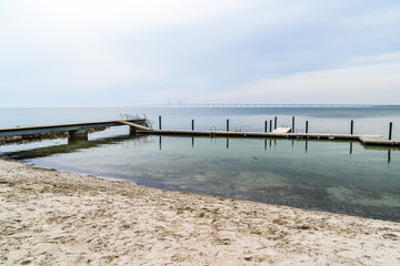 Obraz premium Kalgshamn, Sweden - A bathing pier on a sandy shore on a calm and foggy day. The Oresund bridge is visible in the distant mist.