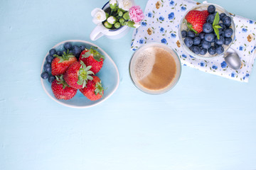 A glass of coffee and pudding chia with blueberries and strawberries for breakfast. Vegetarian healthy food. The flowers in the vase. Blue background. Napkin with flowers. Bright colors. View from abo
