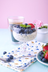 A glass of coffee and pudding chia with blueberries and strawberries for breakfast. Vegetarian food. A small bouquet of flowers, a blue and pink background. Bright colors