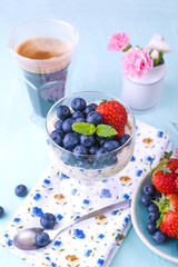 A glass of coffee and pudding chia with blueberries and strawberries for breakfast. Vegetarian healthy food. Blue background. Napkin with flowers and flowers in a vase. Bright colors