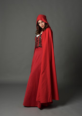 Naklejka premium full length portrait of woman wearing red fantasy costume with cloak, standing pose on grey studio background.