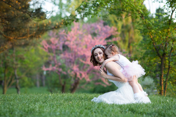 Mom and daughter are two years old sitting on the grass in the park