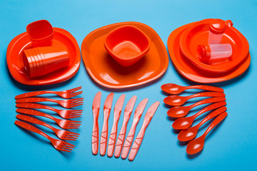 a set of reusable plastic dishes of red color is decomposed on a blue background, a set of dishes