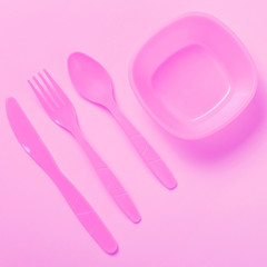 pink plastic utensils on a yellow background, spoon, fork and knife