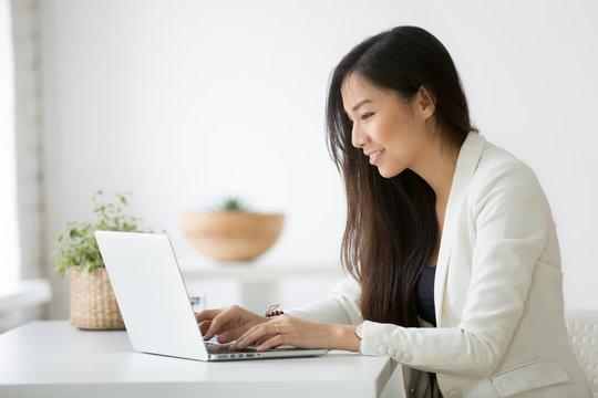 Smiling young asian businesswoman using computer at home office workplace, happy korean employee working on laptop, attractive japanese or chinese woman student studying communicating online with pc