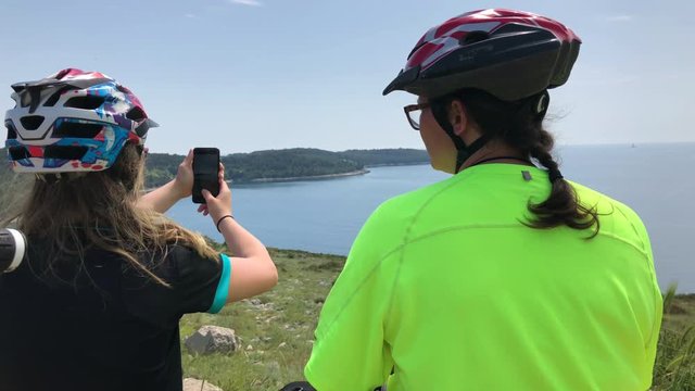 Mother and daughter on mountain bikes taking photos with a smartphone on the top of the mountain trail