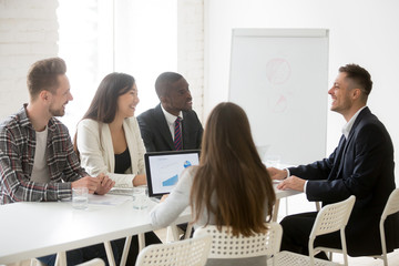 Smiling ceo talking to multiracial team at office meeting, friendly executive discussing good news...