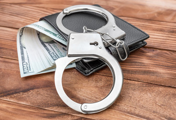 Obraz premium Handcuffs and wallet with money on the wooden table.