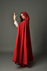 Naklejka premium full length portrait of woman wearing red fantasy costume with cloak, standing pose on grey studio background.
